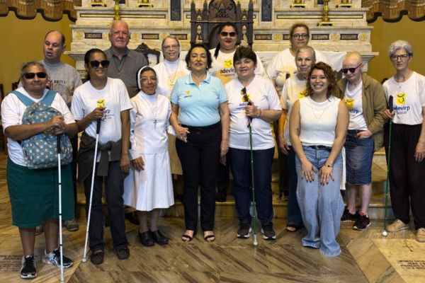Um grupo com 14 pessoas, posam para a foto à frente do altar dos santos: São Pedro, São Sebastião e São Pedro. As pessoas são educandos e colaboradores da adevirp, professora Marlene e a guia da visita, Vitória.